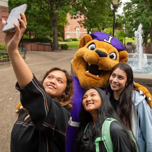 Three female students taking a selfie with Mack the Wildcat.